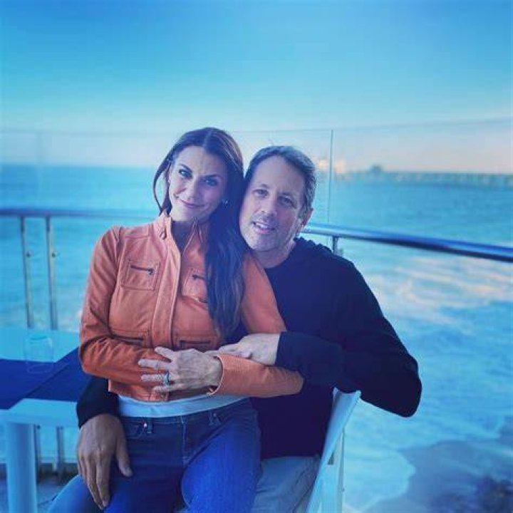 Michael Hess hugging his wife Samantha Harris in an orange jacket and blue jeans.